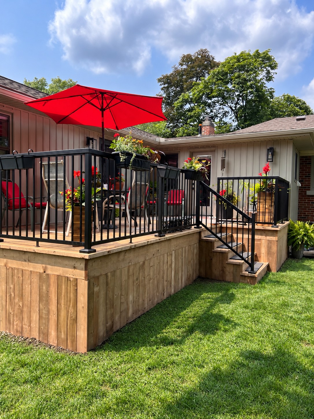 A raised wood deck, black railing and steps into the backyard.