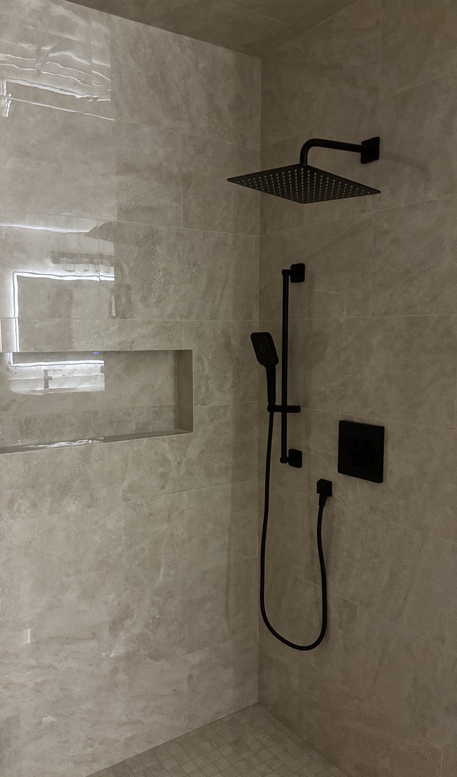 Large-format shower tile, a recessed niche and matte black fixtures.
