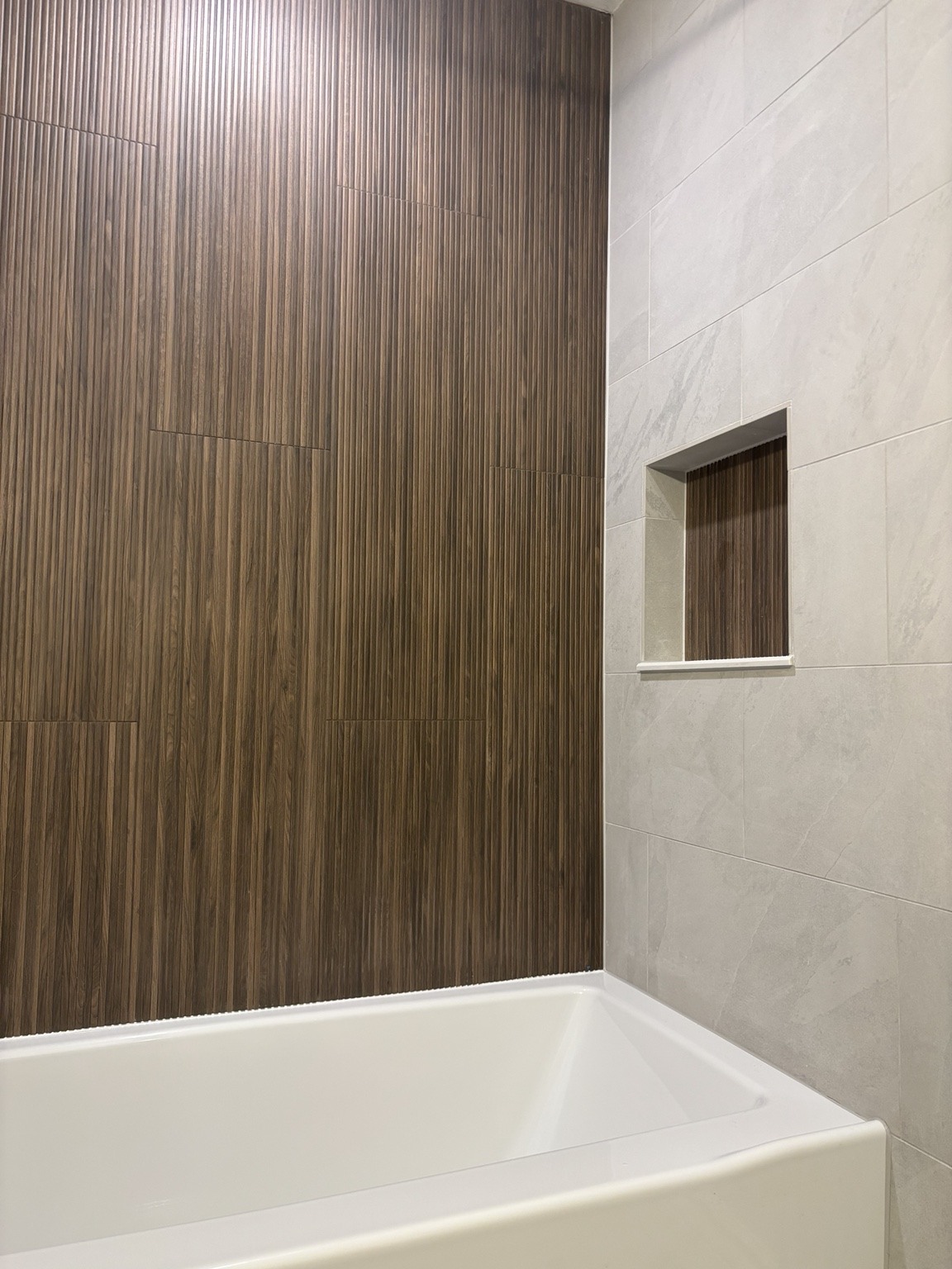 Wood-look feature tile paired with a light tiled tub surround.