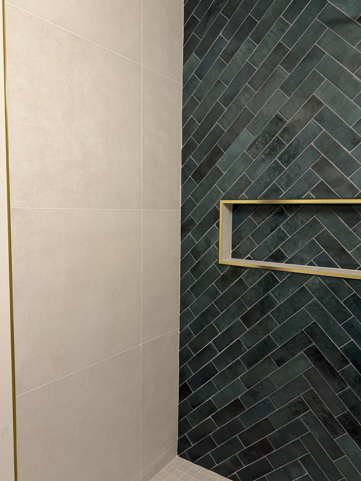Deep green herringbone tile and a gold-trimmed shower niche.
